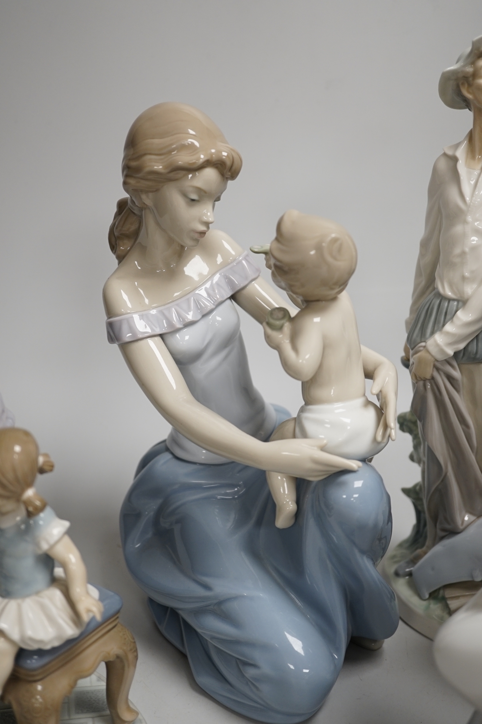 A large Lladro figure of a seated mother and child, a pierrot and ballerina, peasant woman and child, a grandmother and child and two others including a Nao example, the largest 30cm high (6)